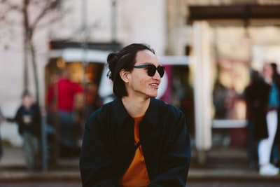 A woman in a black jacket, wearing an orange scarf and black sunglasses